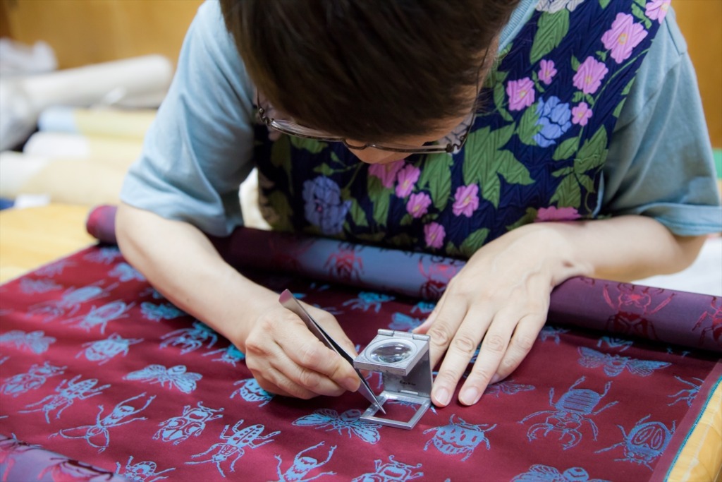 西陣織 金襴が織りあがった後にする検反作業の様子。拡大鏡を使って丁寧に反物をチェックしていきます。